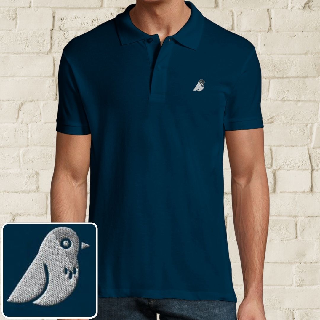 Birdie Polo in Denim on a light wooden floor lying next to headphones and golf shoes.