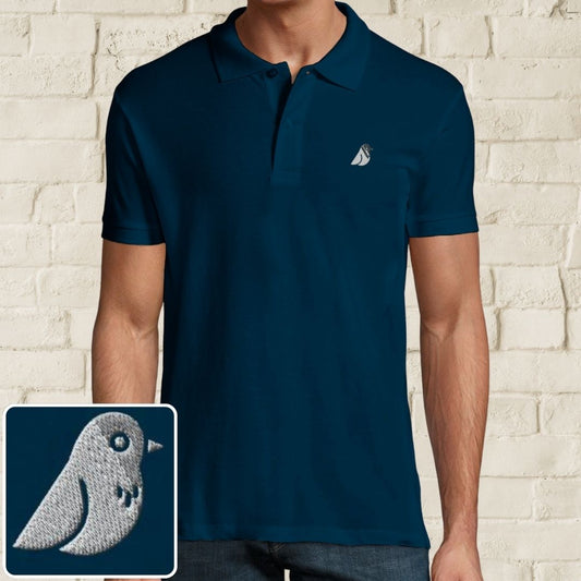 Birdie Polo in Denim on a light wooden floor lying next to headphones and golf shoes.