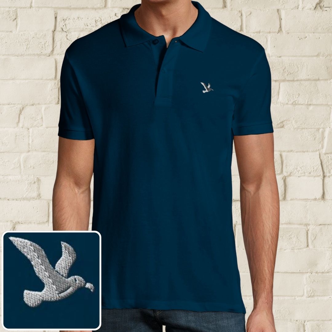Albatross Polo in Denim on a light wooden floor lying next to headphones and golf shoes.