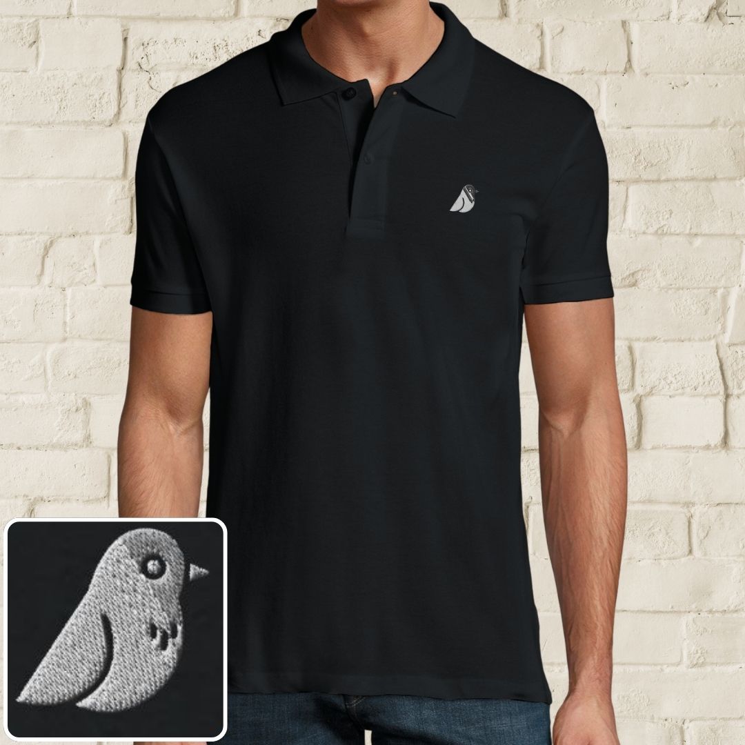 Birdie Polo in Black on a light wooden floor lying next to headphones and golf shoes.
