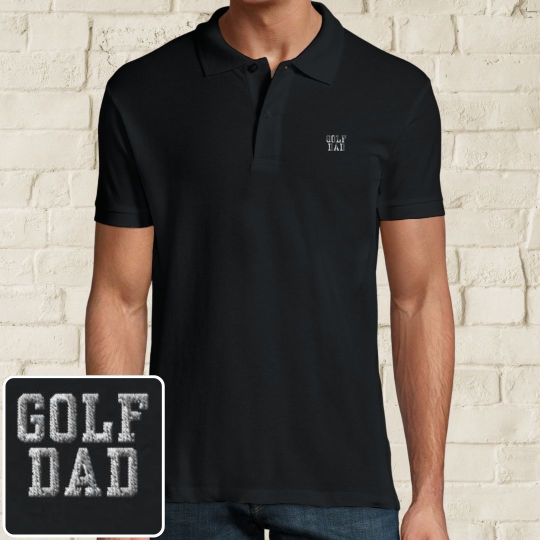 Golf Dad Polo in Black on a light wooden floor lying next to headphones and golf shoes.