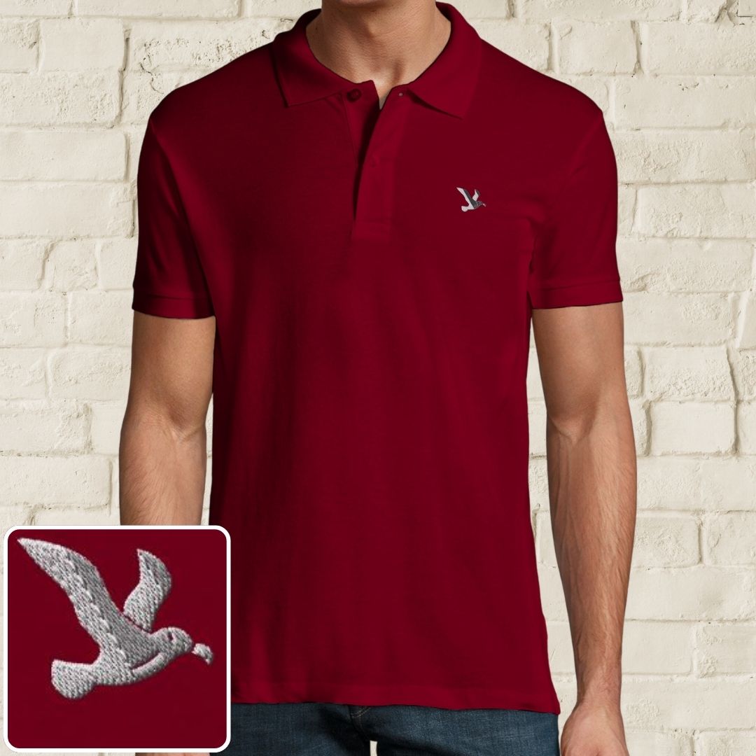 Albatross Polo in Maroon on a light wooden floor lying next to headphones and golf shoes.