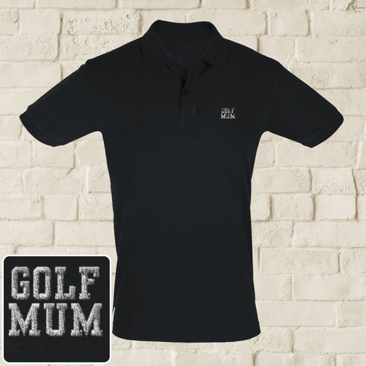 Golf Mum Polo in Black on a light wooden floor lying next to headphones and golf shoes.