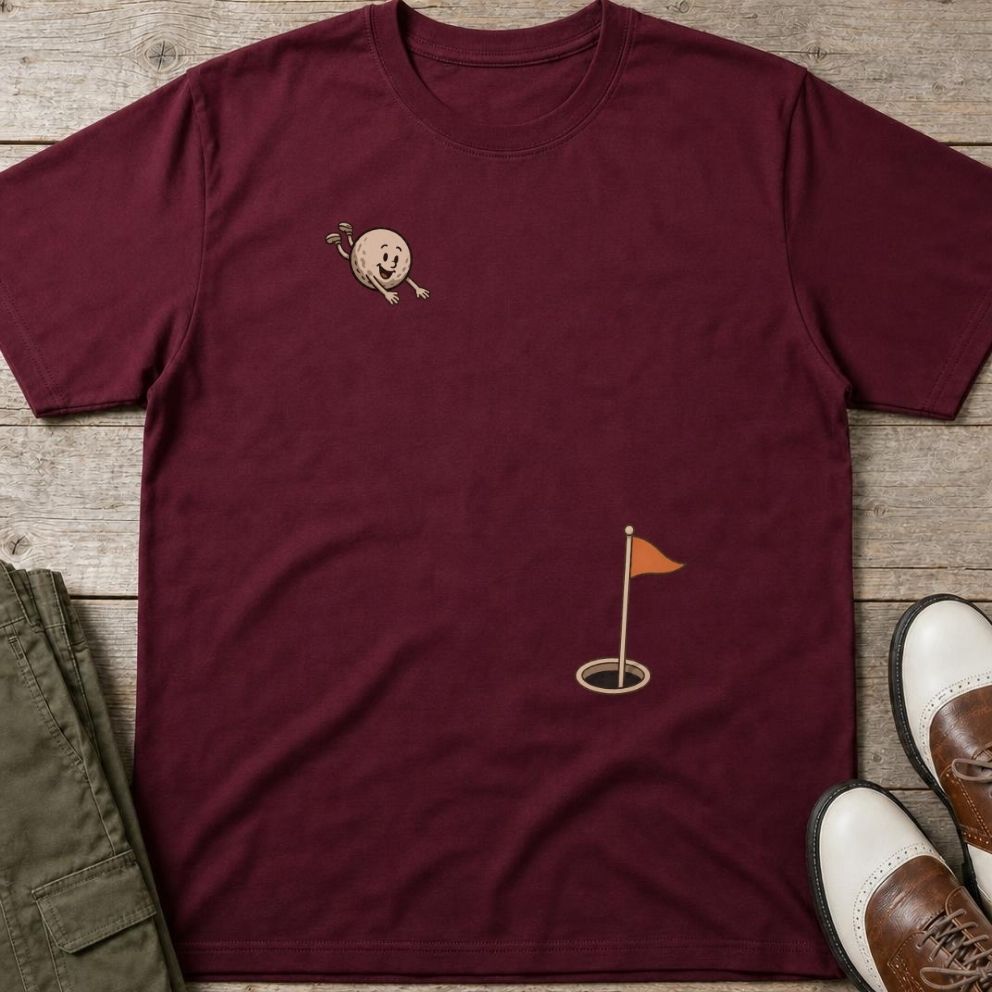 Flying Golf Ball T-Shirt in Maroon lying on a plain floor. T-shirt is a unisex cut and 100 per cent cotton.