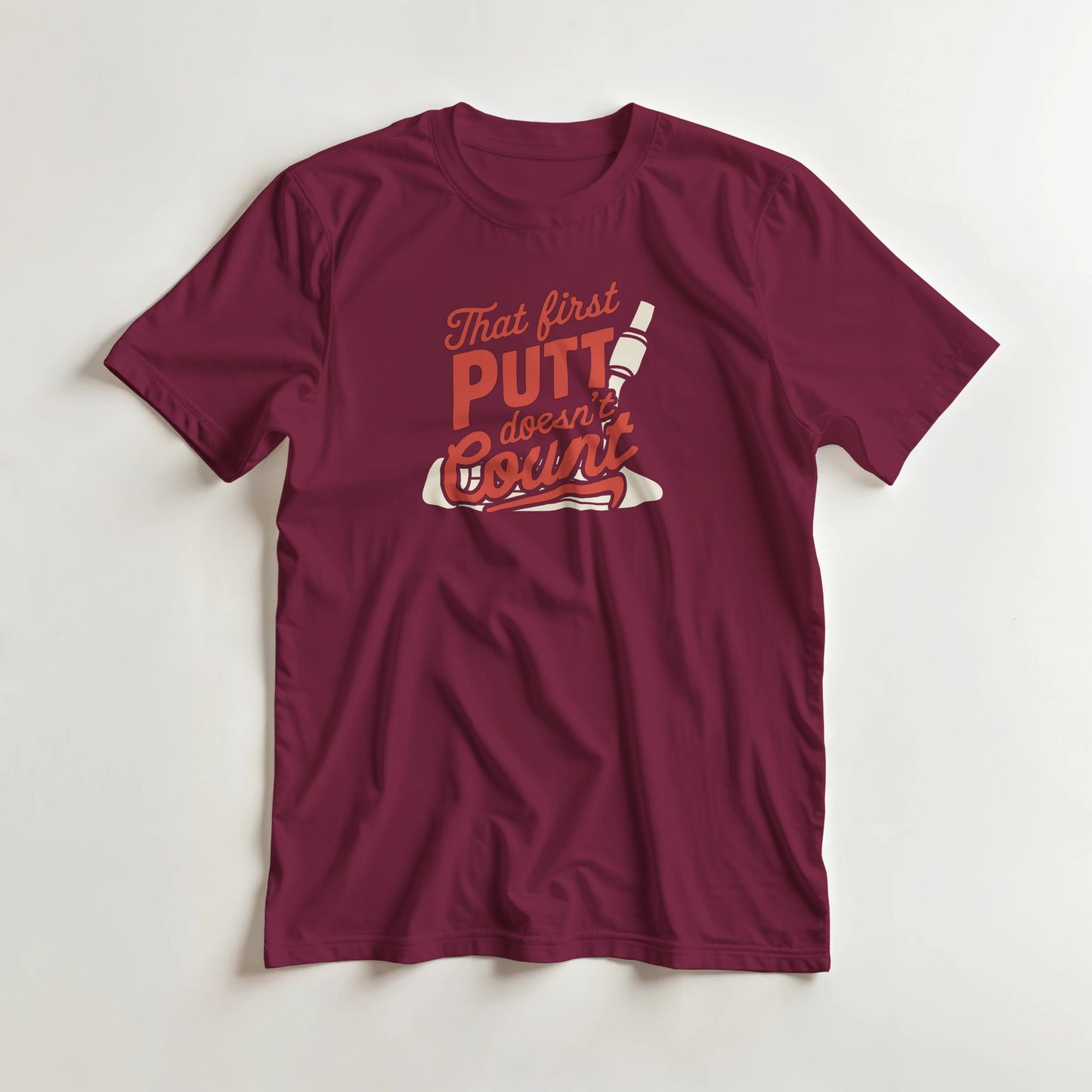 First Putt T-Shirt in Maroon lying on a plain floor. T-shirt is a unisex cut and 100 per cent cotton.