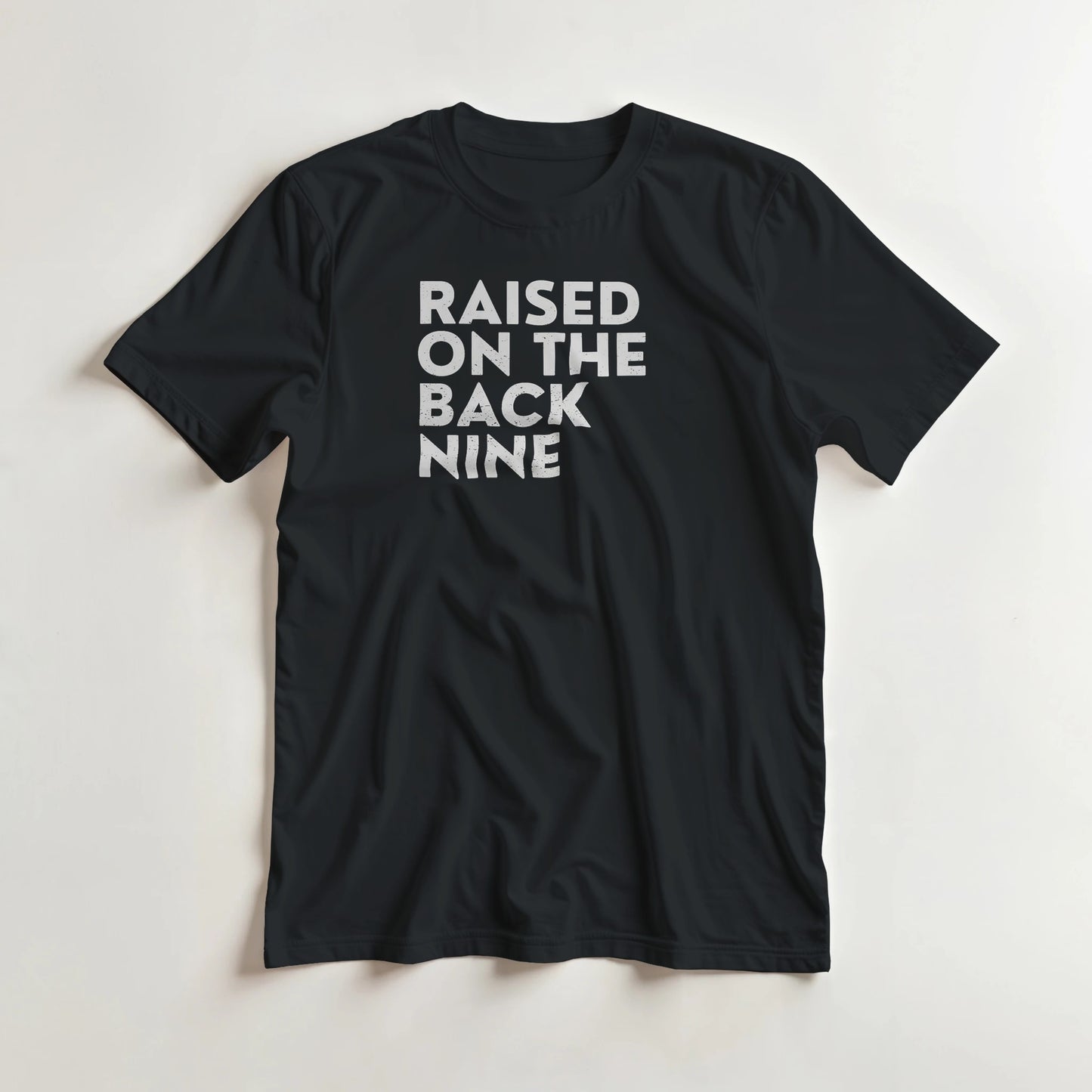 Raised On T-Shirt in Black lying on a plain floor. T-shirt is a unisex cut and 100 per cent cotton.