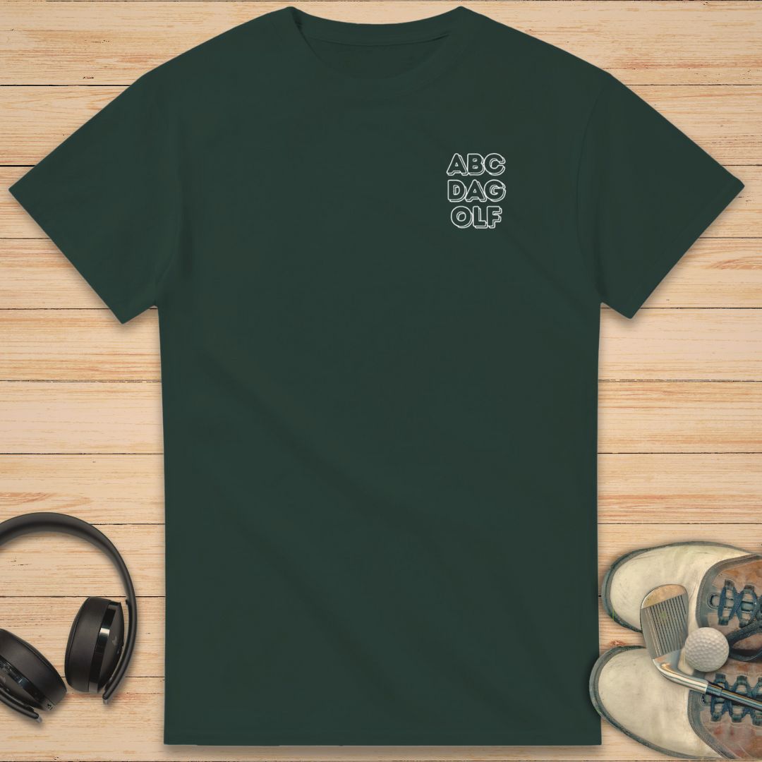 ABC Da Golf T-Shirt in Forest Green on a light wooden floor lying next to headphones and golf shoes.