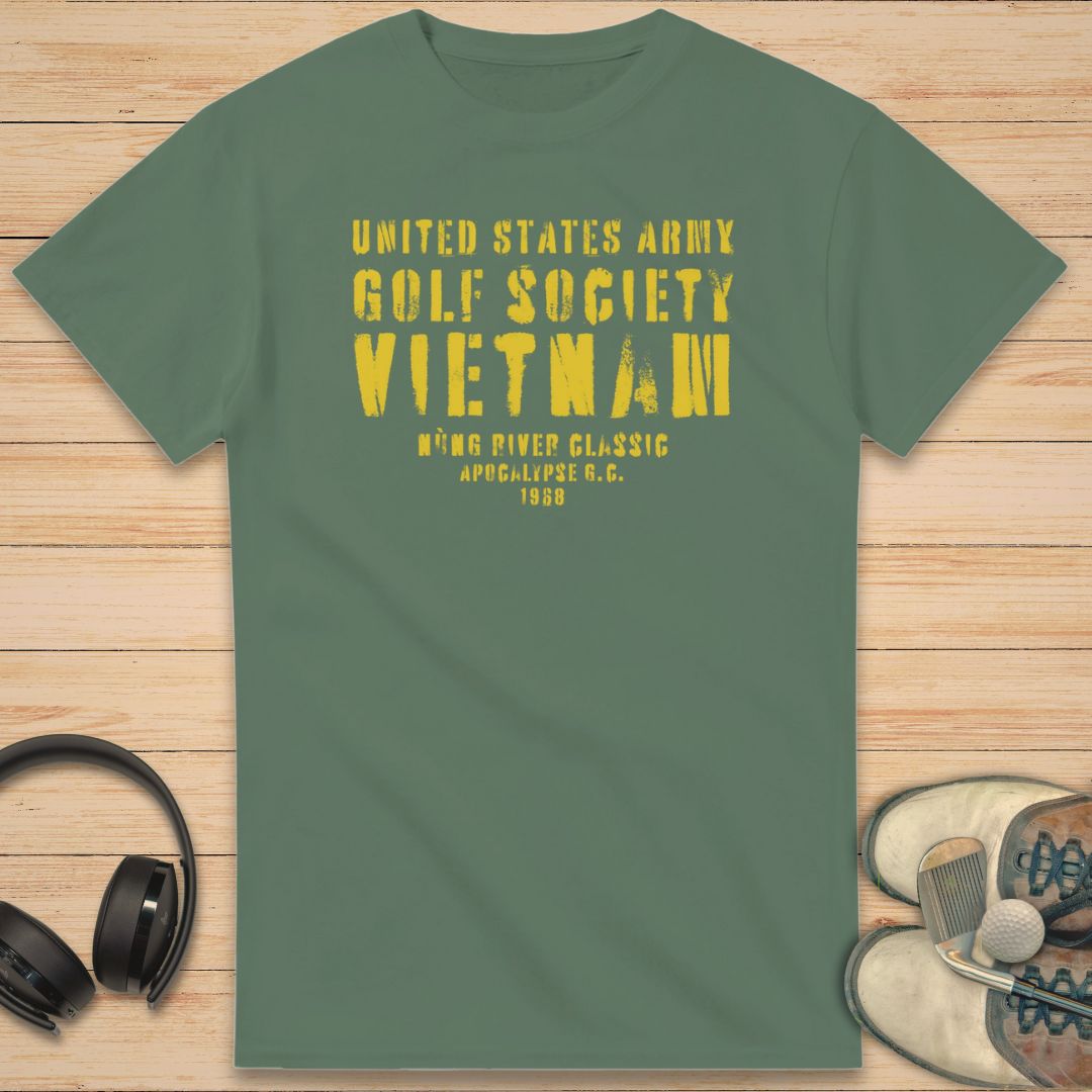 Apocalypse G.C. T-Shirt in Military Green on a light wooden floor lying next to headphones and golf shoes.