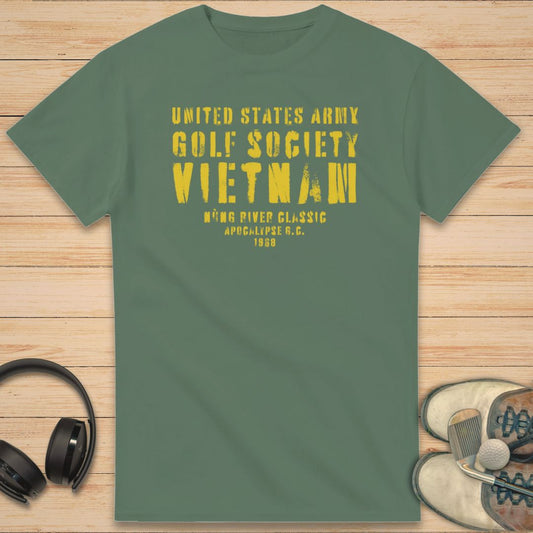Apocalypse G.C. T-Shirt in Military Green on a light wooden floor lying next to headphones and golf shoes.