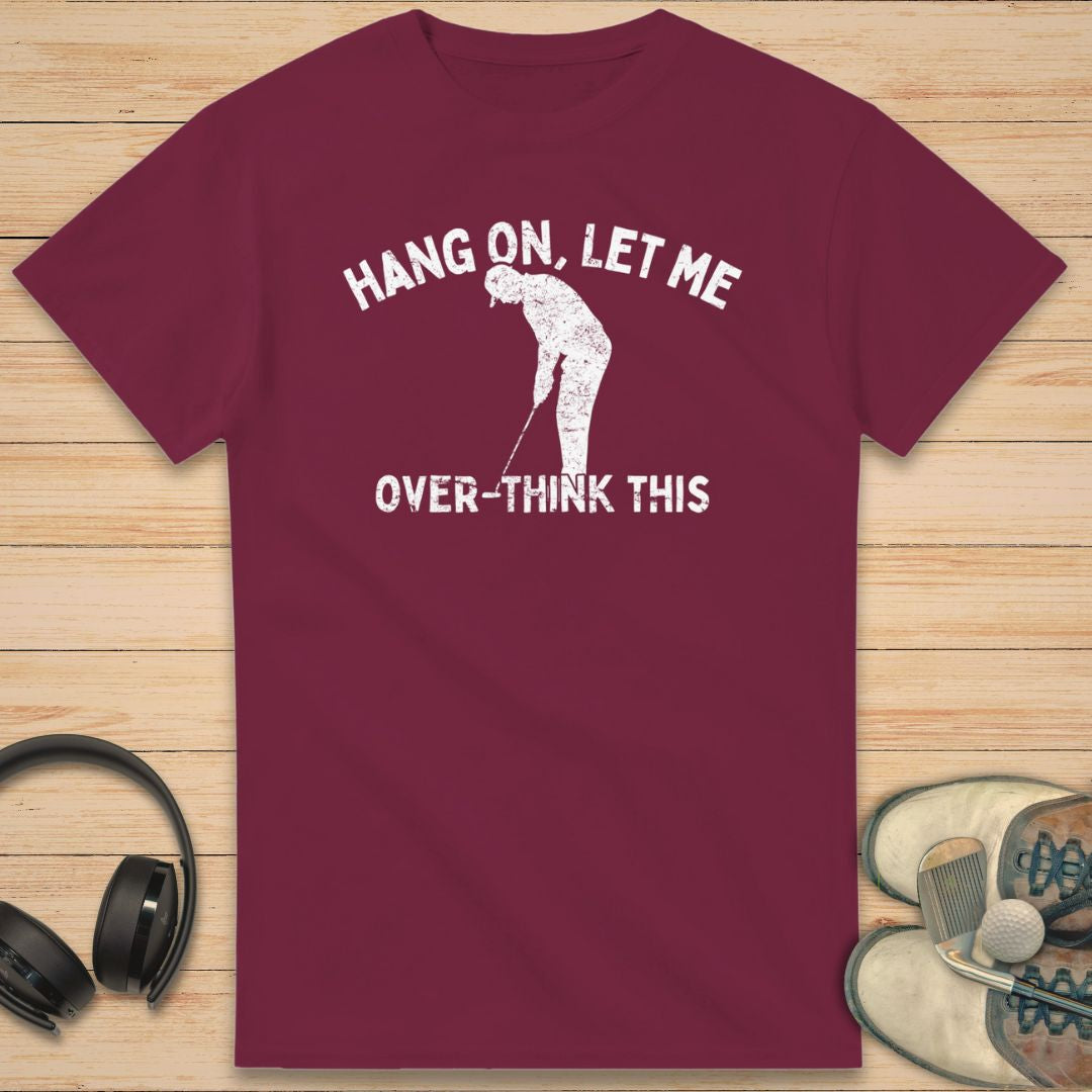 Over-Think T-Shirt in Maroon on a light wooden floor lying next to headphones and golf shoes.