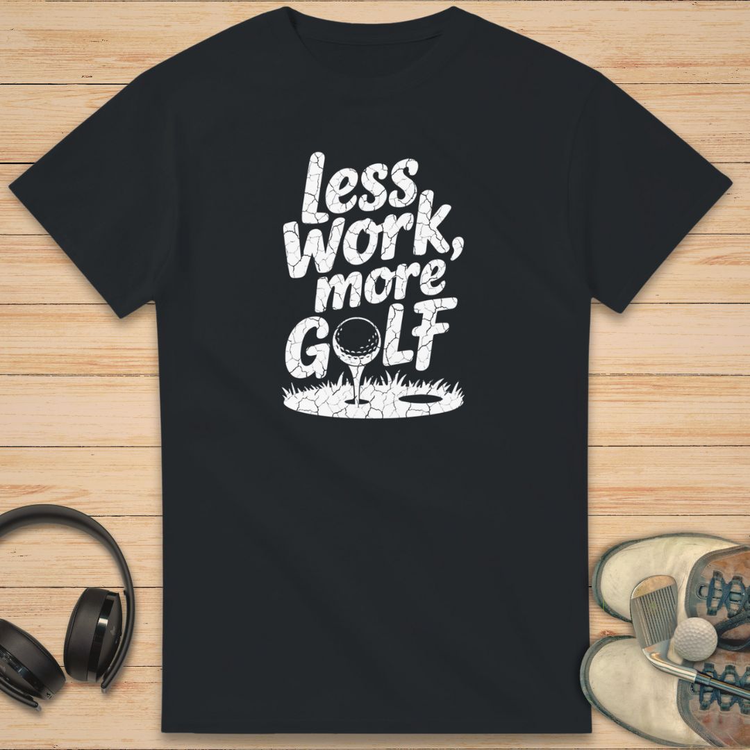 More Golf T-Shirt in Black on a light wooden floor lying next to headphones and golf shoes.