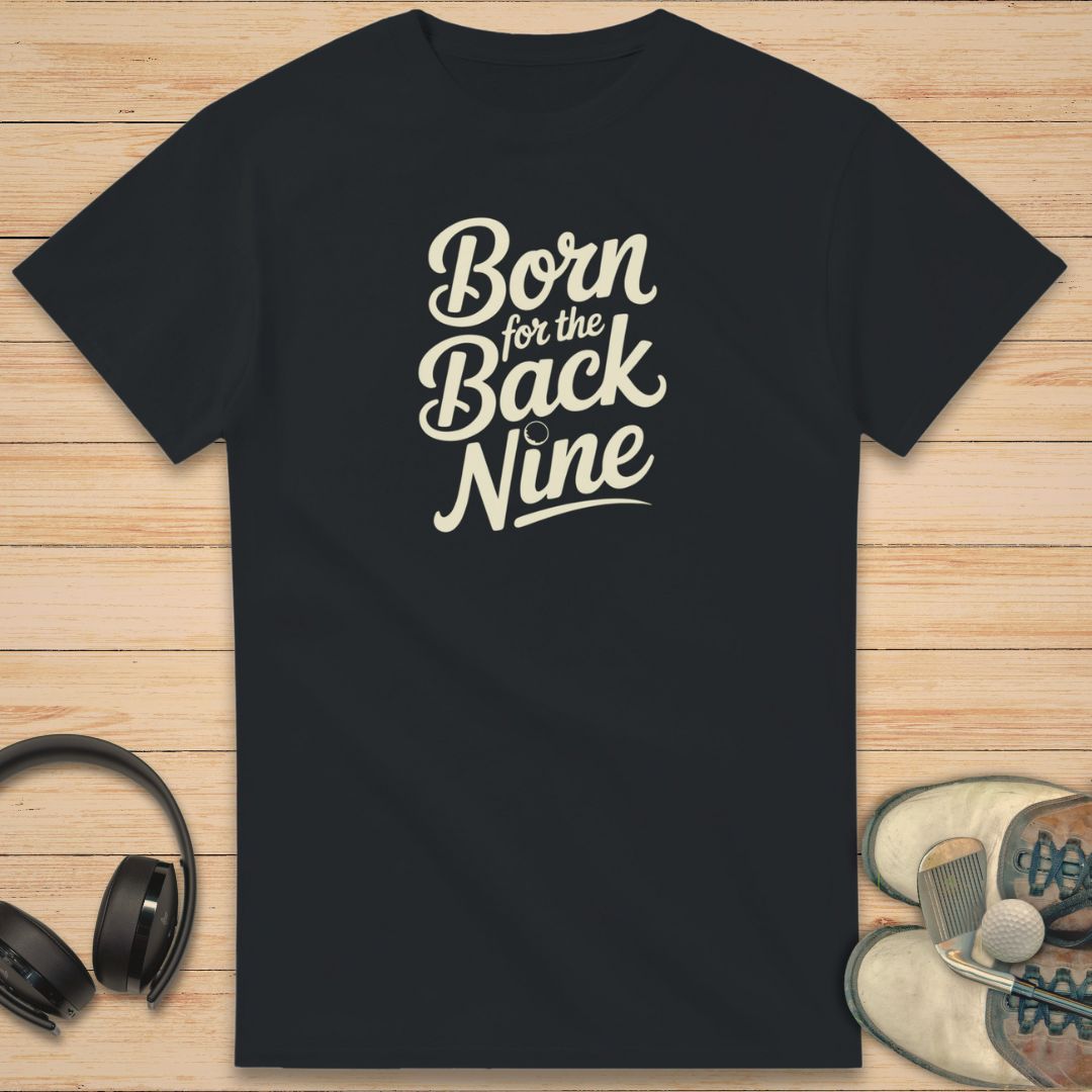 Back Nine T-Shirt in Black on a light wooden floor lying next to headphones and golf shoes.