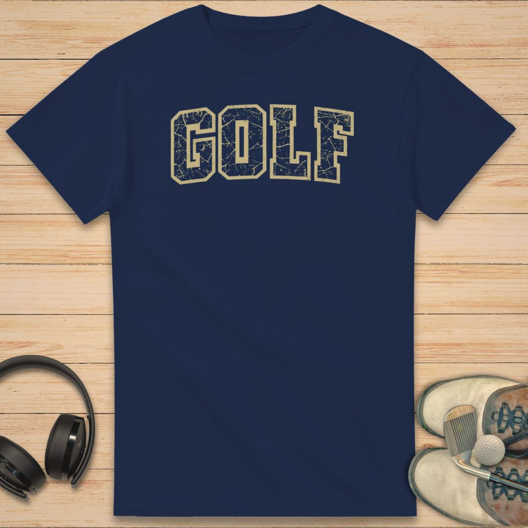 Varsity Golf T-Shirt in Navy on a light wooden floor lying next to headphones and golf shoes.