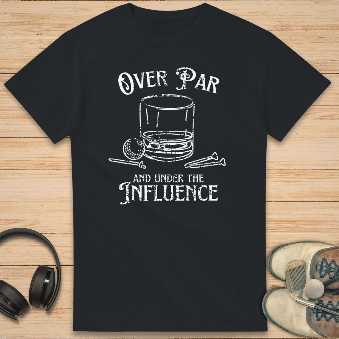 Over Par T-Shirt in Black on a light wooden floor lying next to headphones and golf shoes.
