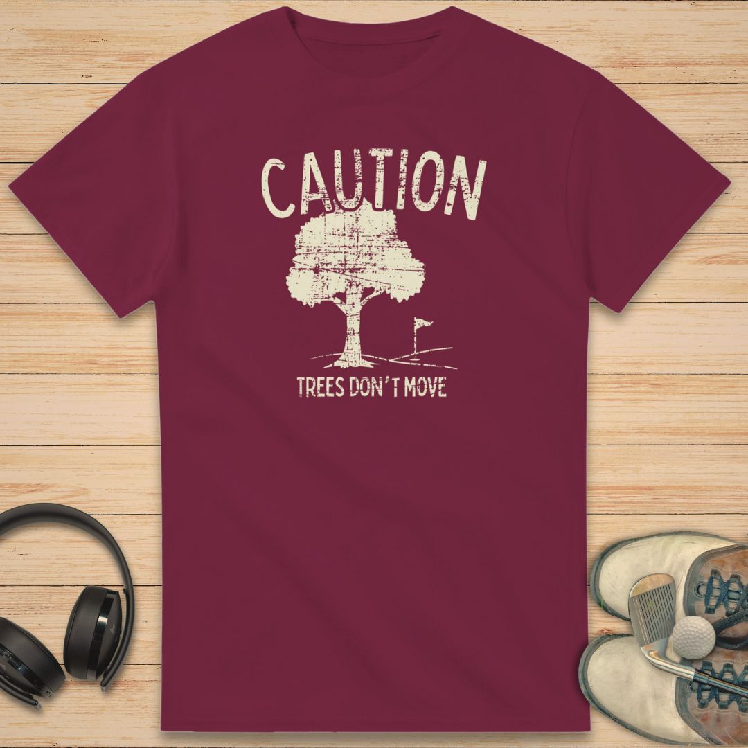 Caution T-Shirt in Maroon on a light wooden floor lying next to headphones and golf shoes.
