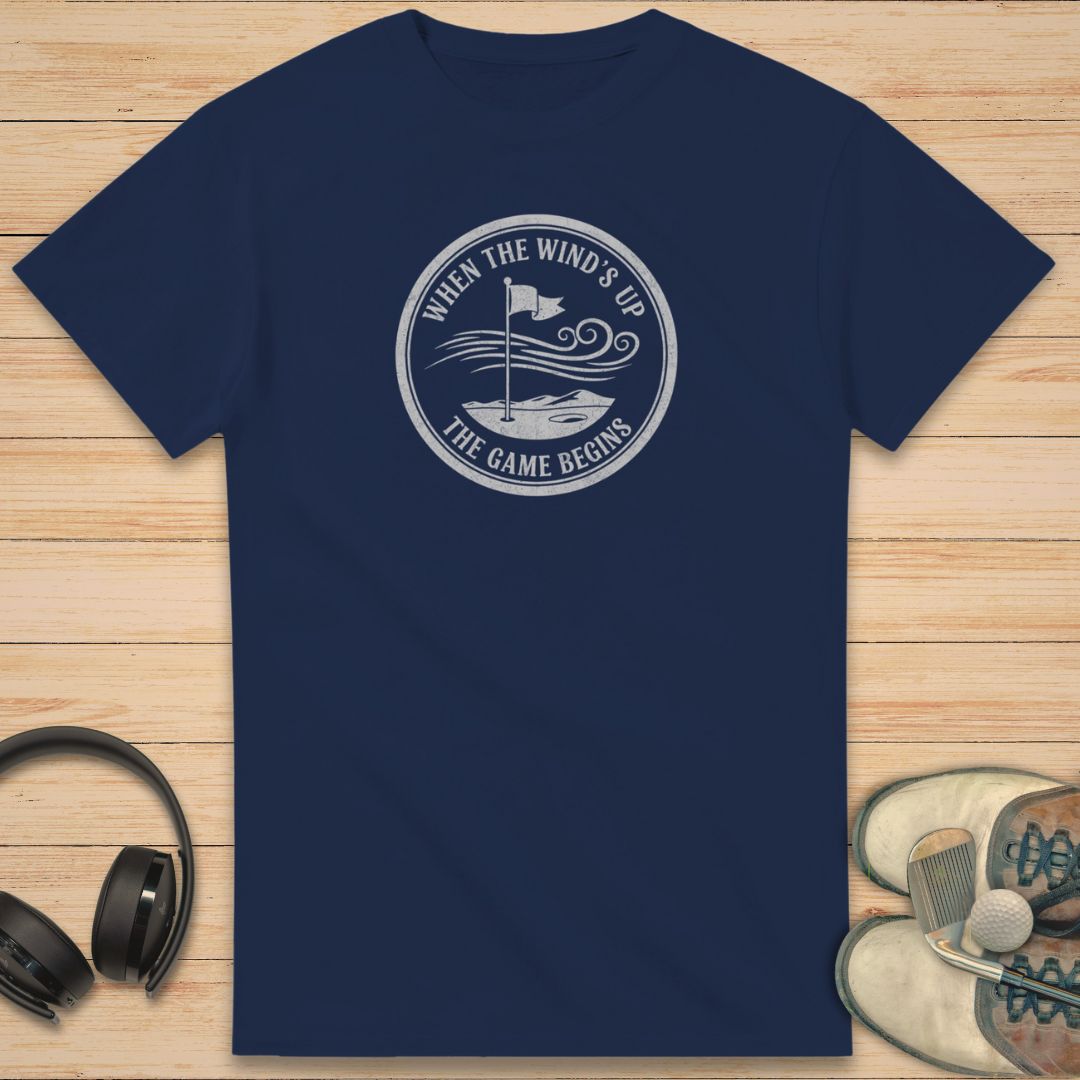 Navy blue t-shirt with a white graphic design on a wooden surface with headphones and shoes.