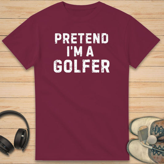 Maroon t-shirt with 'Pretend I'm a Golfer' text on a wooden surface with headphones and shoes.