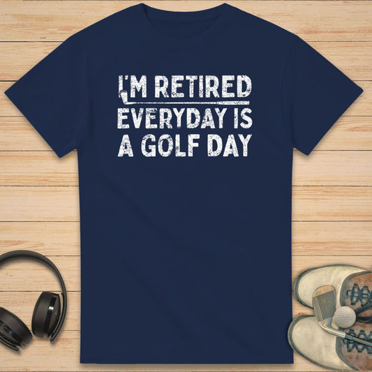 A Golf Day T-Shirt in Navy on a light wooden floor lying next to headphones and golf shoes.