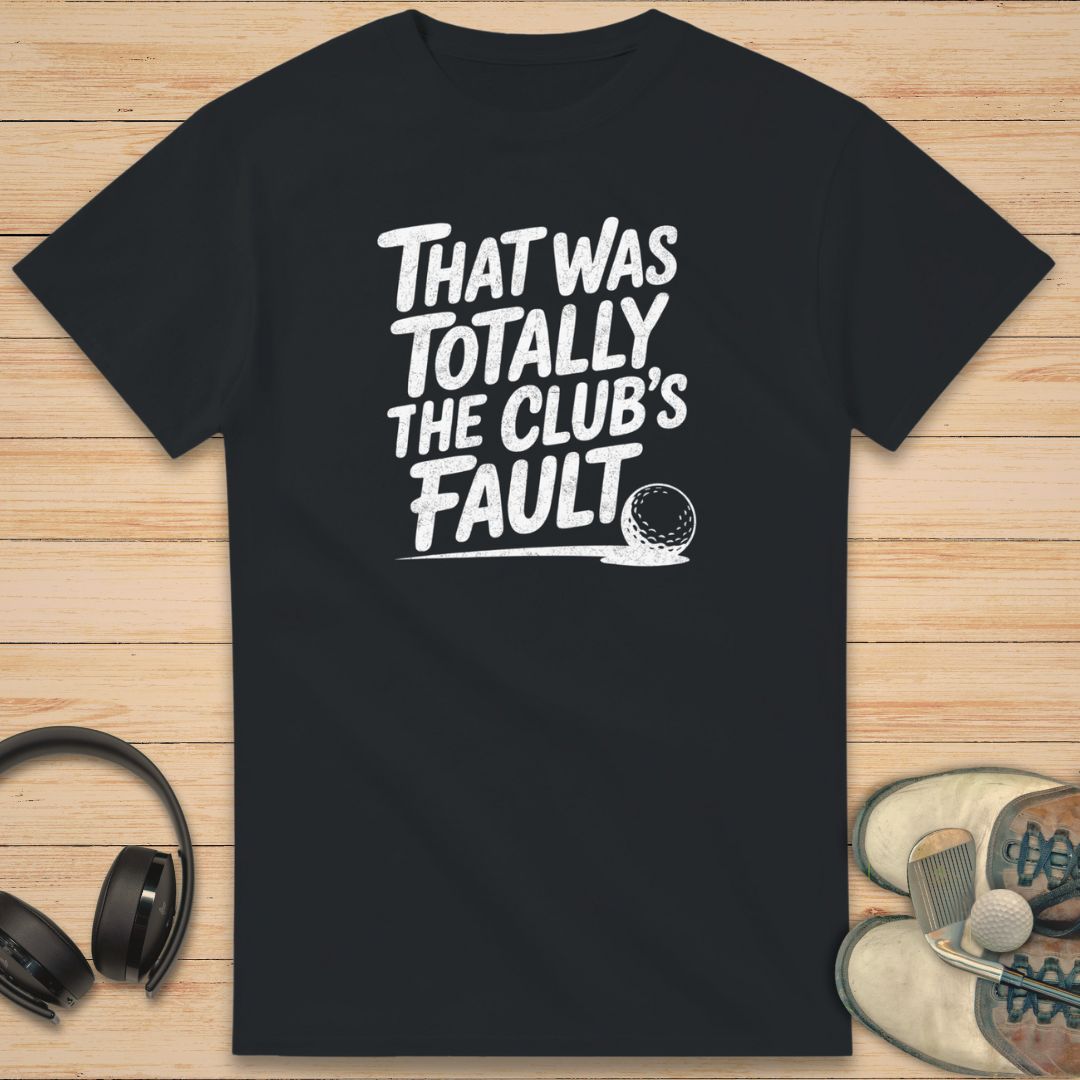 Club's Fault T-Shirt in on a light wooden floor lying next to headphones and golf shoes.