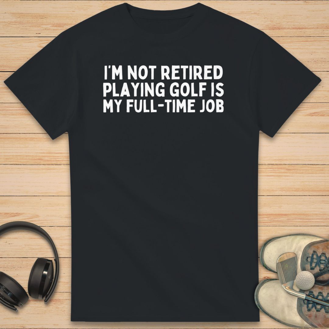 Full-Time Job T-Shirt in Black on a light wooden floor lying next to headphones and golf shoes.