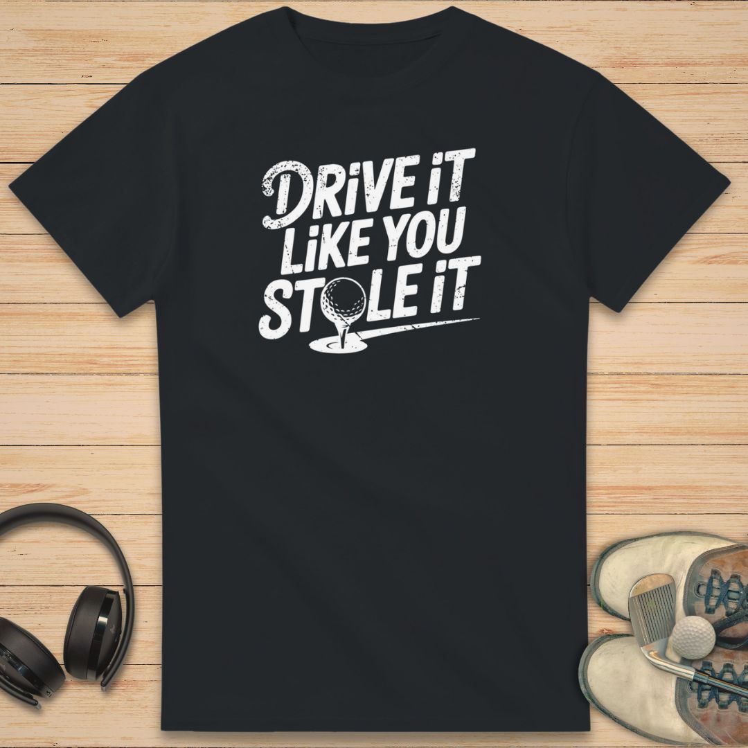 Stole It T-Shirt in Black on a light wooden floor lying next to headphones and golf shoes.