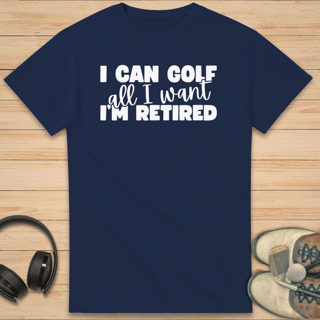 Golf All I Want T-Shirt in Navy on a light wooden floor lying next to headphones and golf shoes.