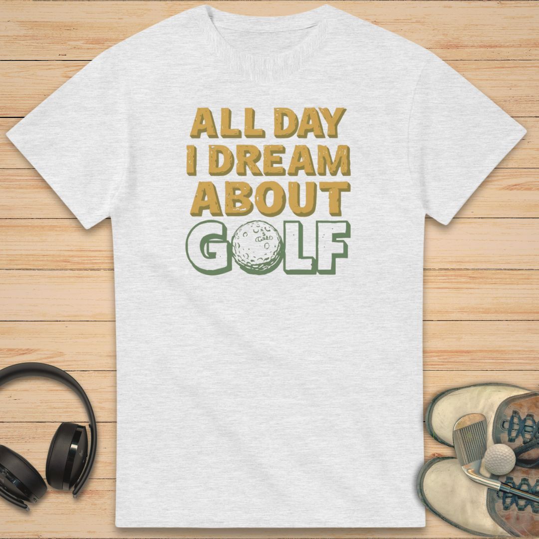 About Golf T-Shirt in Ash on a light wooden floor lying next to headphones and golf shoes.