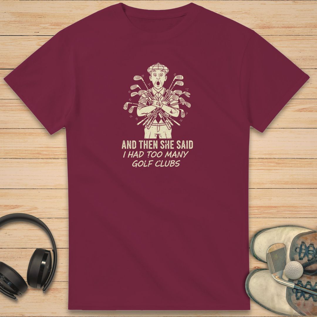 She Said T-Shirt in Maroon on a light wooden floor lying next to headphones and golf shoes.