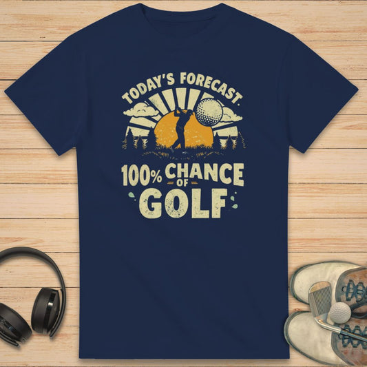 100% Chance of Golf T-Shirt in Navy on a light wooden floor lying next to headphones and golf shoes.