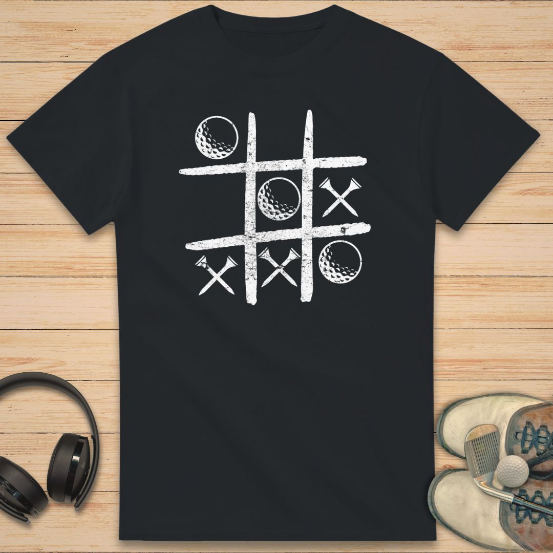 Balls And Tees T-Shirt in Black on a light wooden floor lying next to headphones and golf shoes.