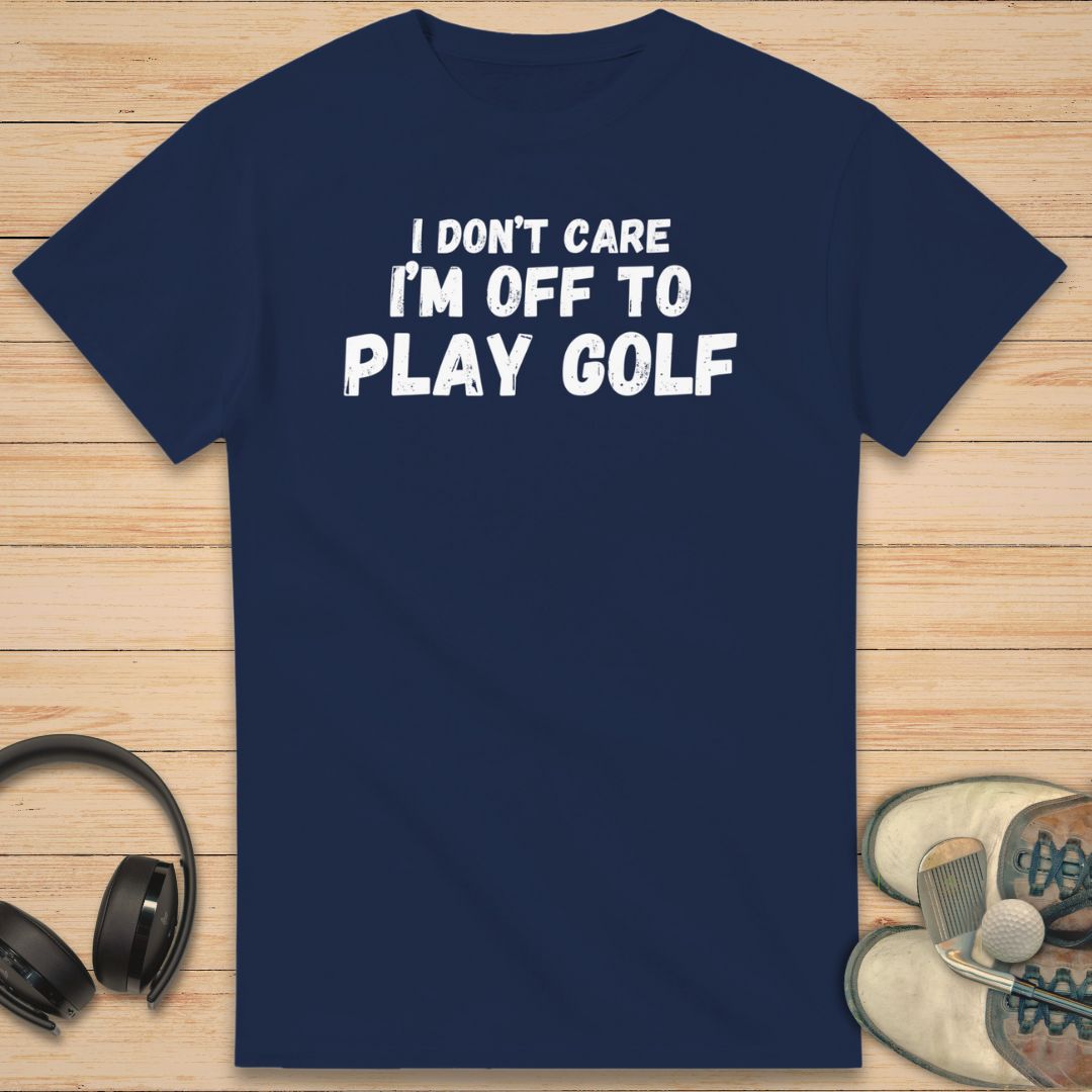 Don't Care T-Shirt in Navy on a light wooden floor lying next to headphones and golf shoes.