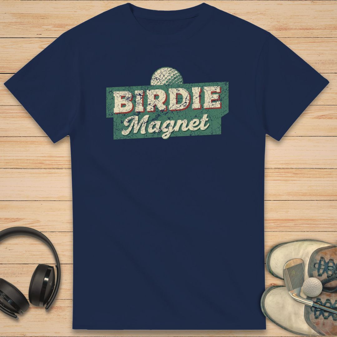 Birdie Magnet T-Shirt in Navy on a light wooden floor lying next to headphones and golf shoes.