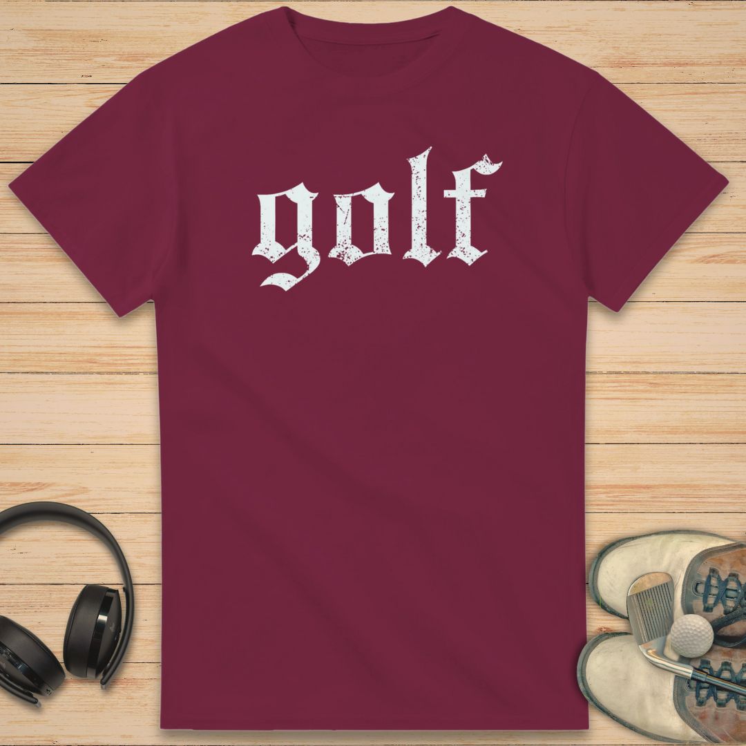 Gothic Golf T-Shirt in Maroon on a light wooden floor lying next to headphones and golf shoes.