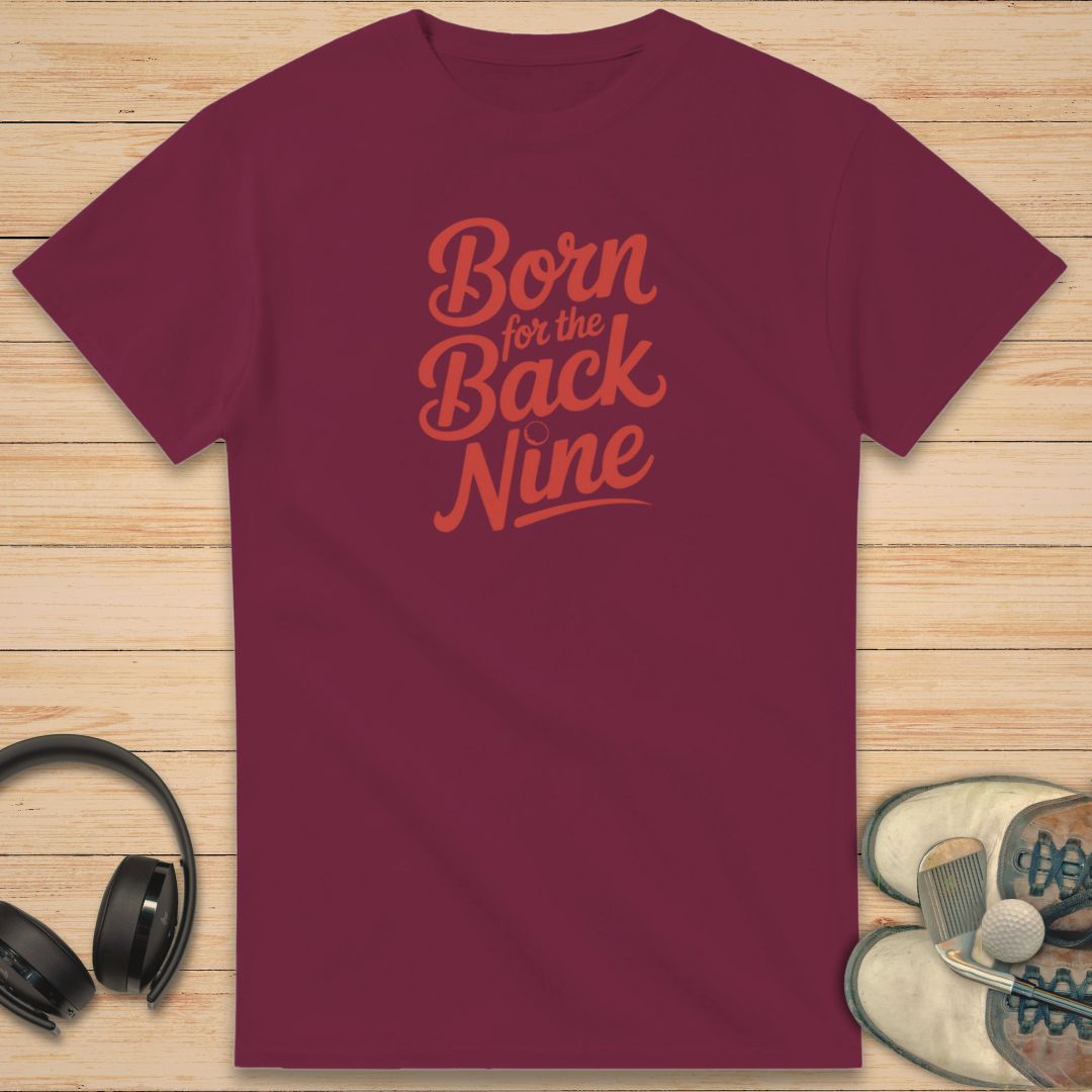 Back Nine T-Shirt in Maroon on a light wooden floor lying next to headphones and golf shoes.