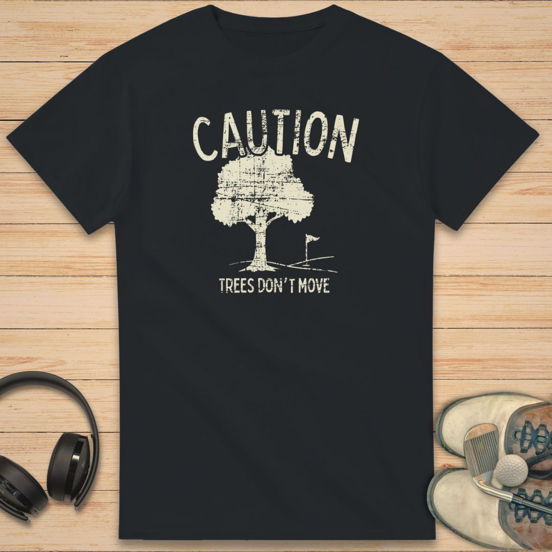 Caution T-Shirt in Black on a light wooden floor lying next to headphones and golf shoes.