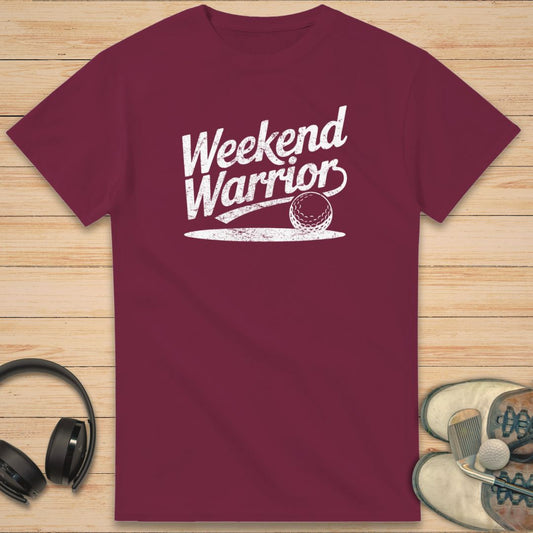 Warrior T-Shirt in Maroon on a light wooden floor lying next to headphones and golf shoes.