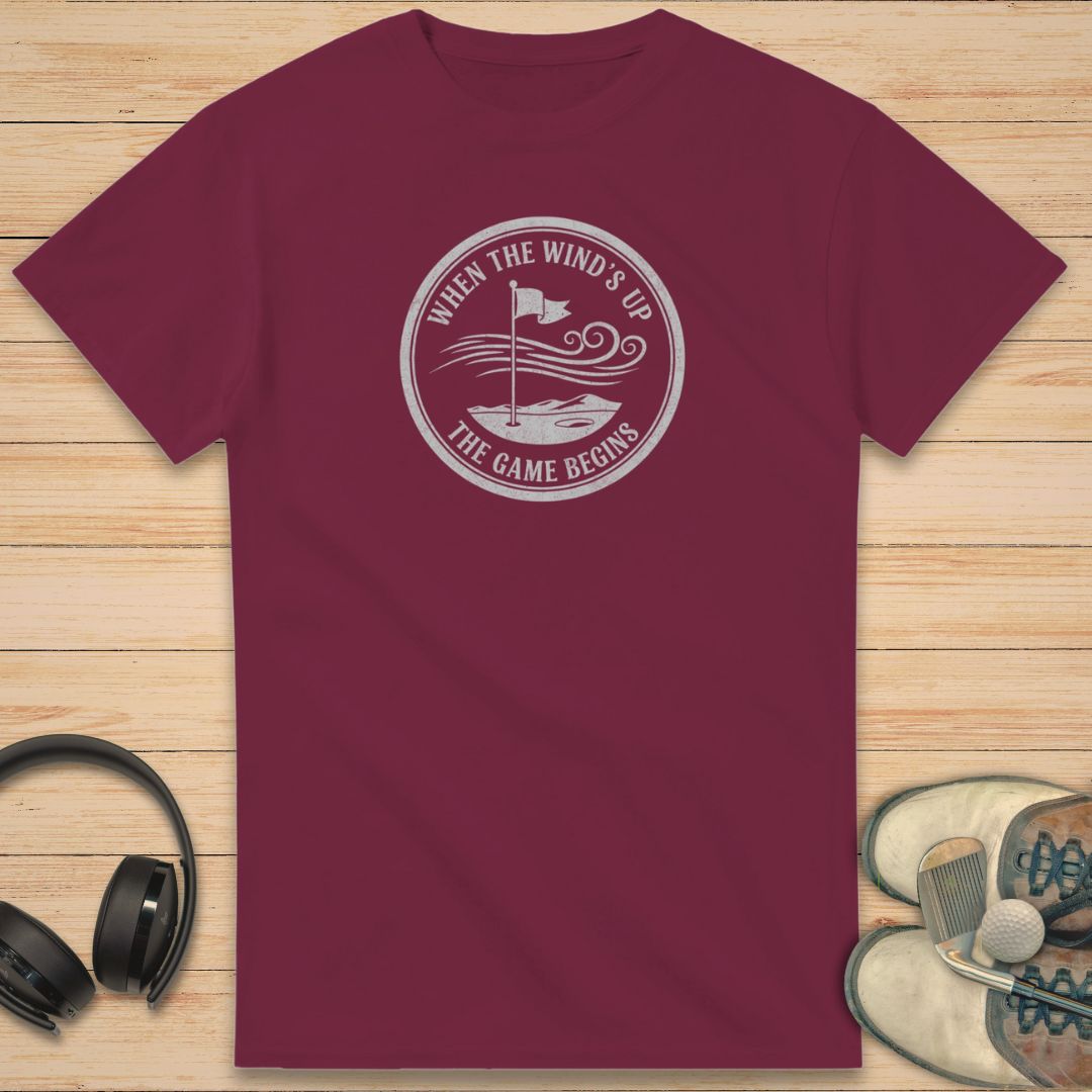 Maroon t-shirt with a white graphic design on a wooden surface with headphones and shoes.