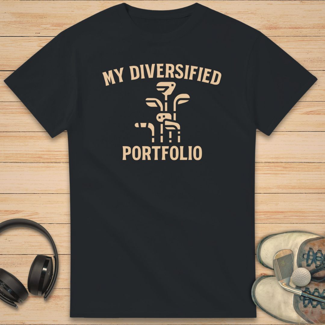 Portfolio T-Shirt in Black on a light wooden floor lying next to headphones and golf shoes.
