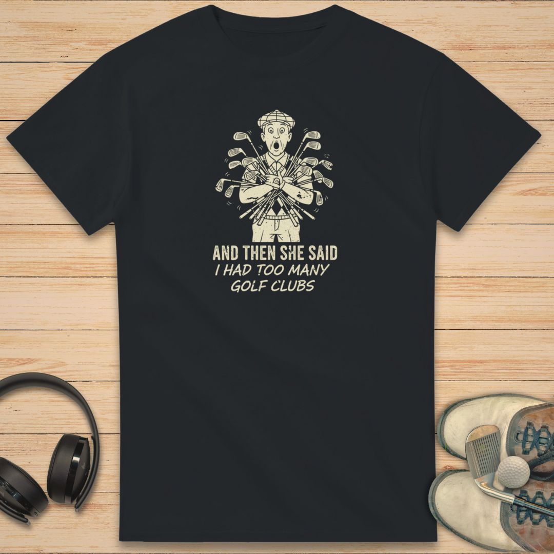 She Said T-Shirt in Black on a light wooden floor lying next to headphones and golf shoes.