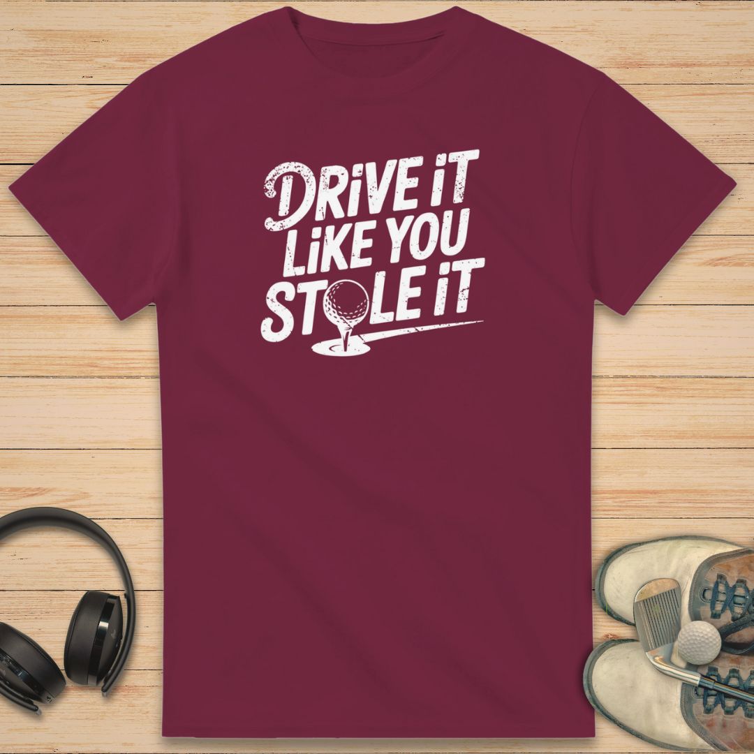 Stole It T-Shirt in Maroon on a light wooden floor lying next to headphones and golf shoes.