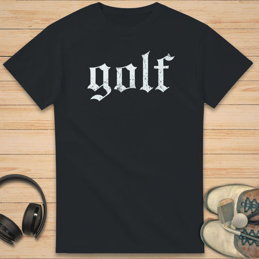 Gothic Golf T-Shirt in Black on a light wooden floor lying next to headphones and golf shoes.