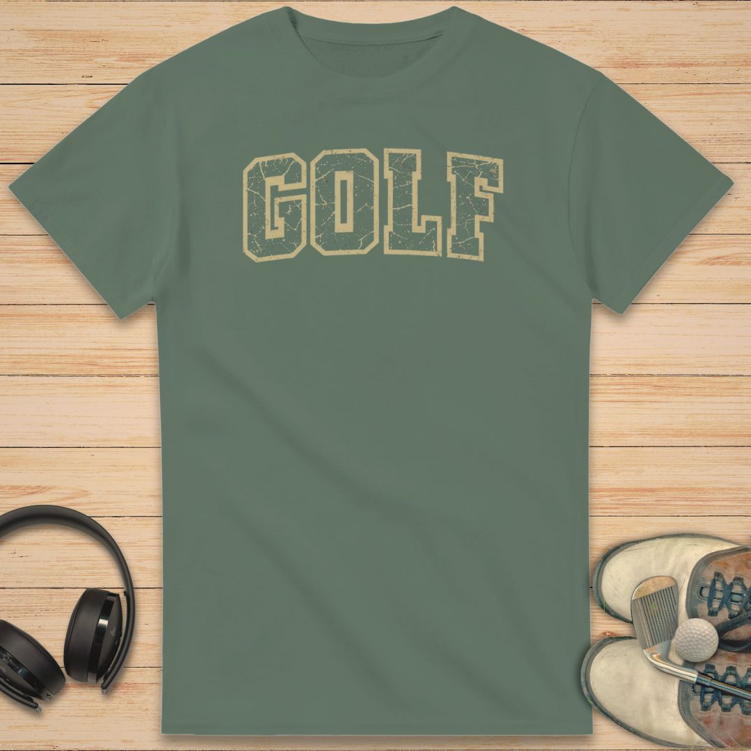 Varsity Golf T-Shirt in Military Green on a light wooden floor lying next to headphones and golf shoes.