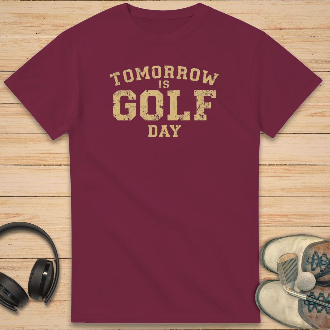 Golf Day T-Shirt in Maroon on a light wooden floor lying next to headphones and golf shoes.