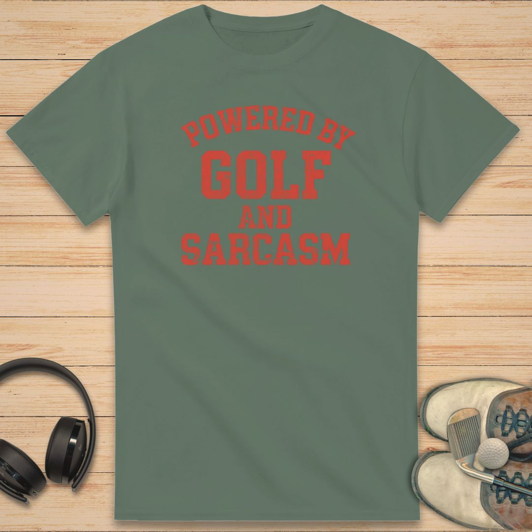 Powered By T-Shirt in Military Green on a light wooden floor lying next to headphones and golf shoes.