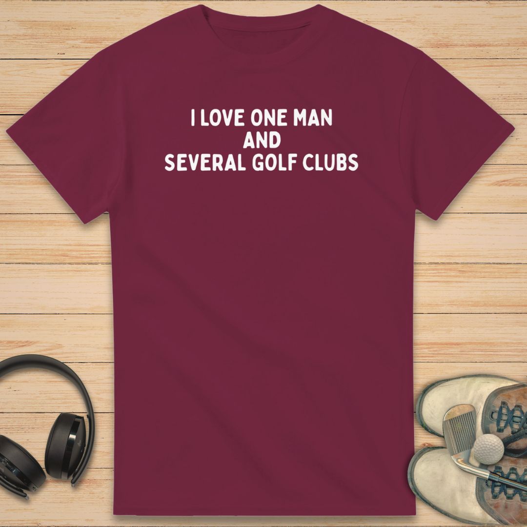 One Man T-Shirt in Maroon on a light wooden floor lying next to headphones and golf shoes.