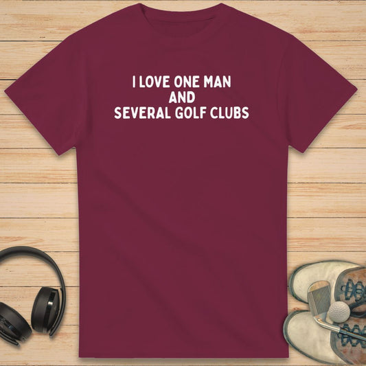One Man T-Shirt in Maroon on a light wooden floor lying next to headphones and golf shoes.
