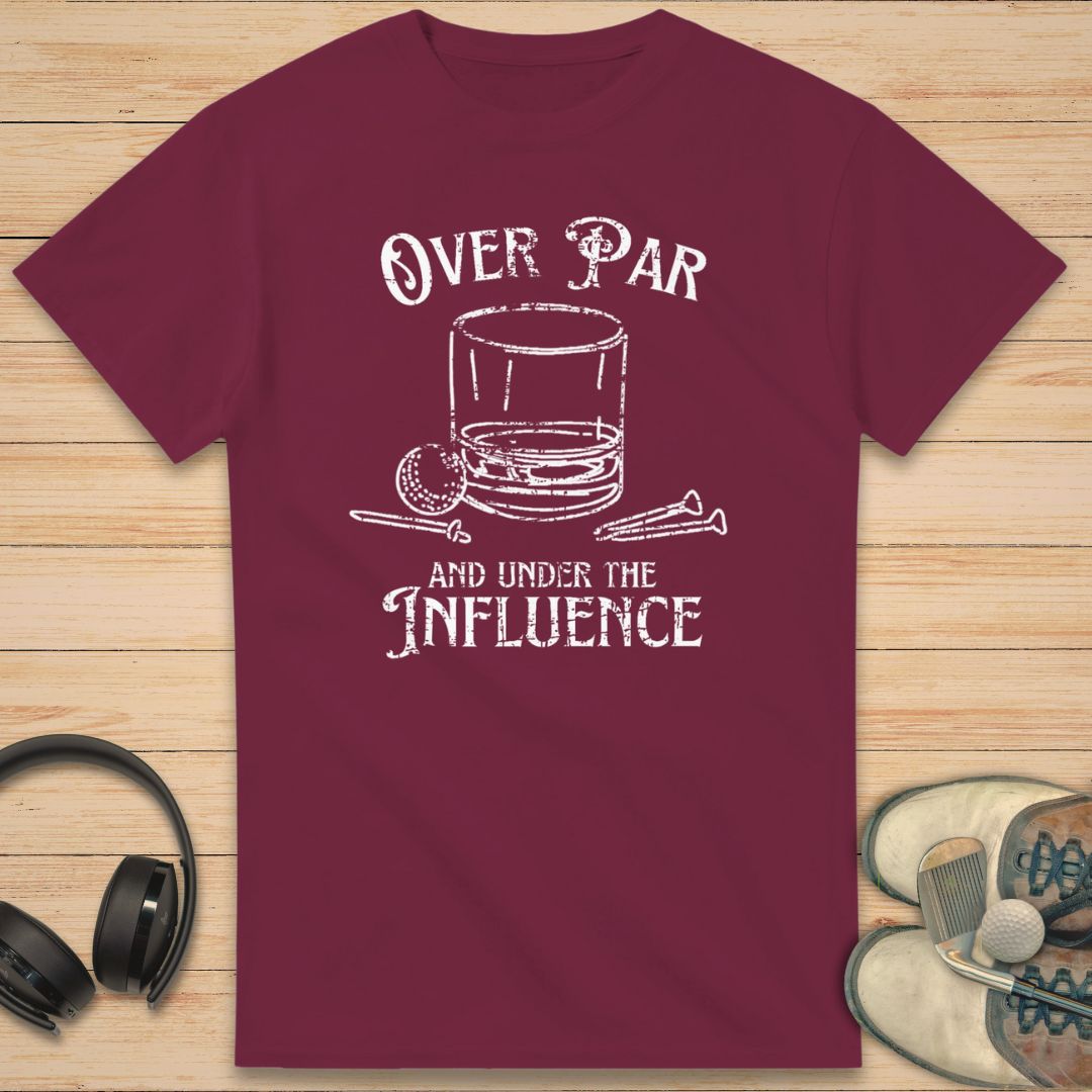 Over Par T-Shirt in Maroon on a light wooden floor lying next to headphones and golf shoes.