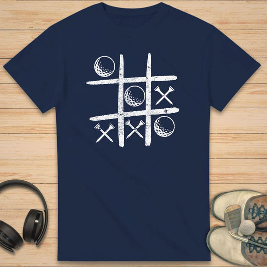 Balls And Tees T-Shirt in Navy on a light wooden floor lying next to headphones and golf shoes.