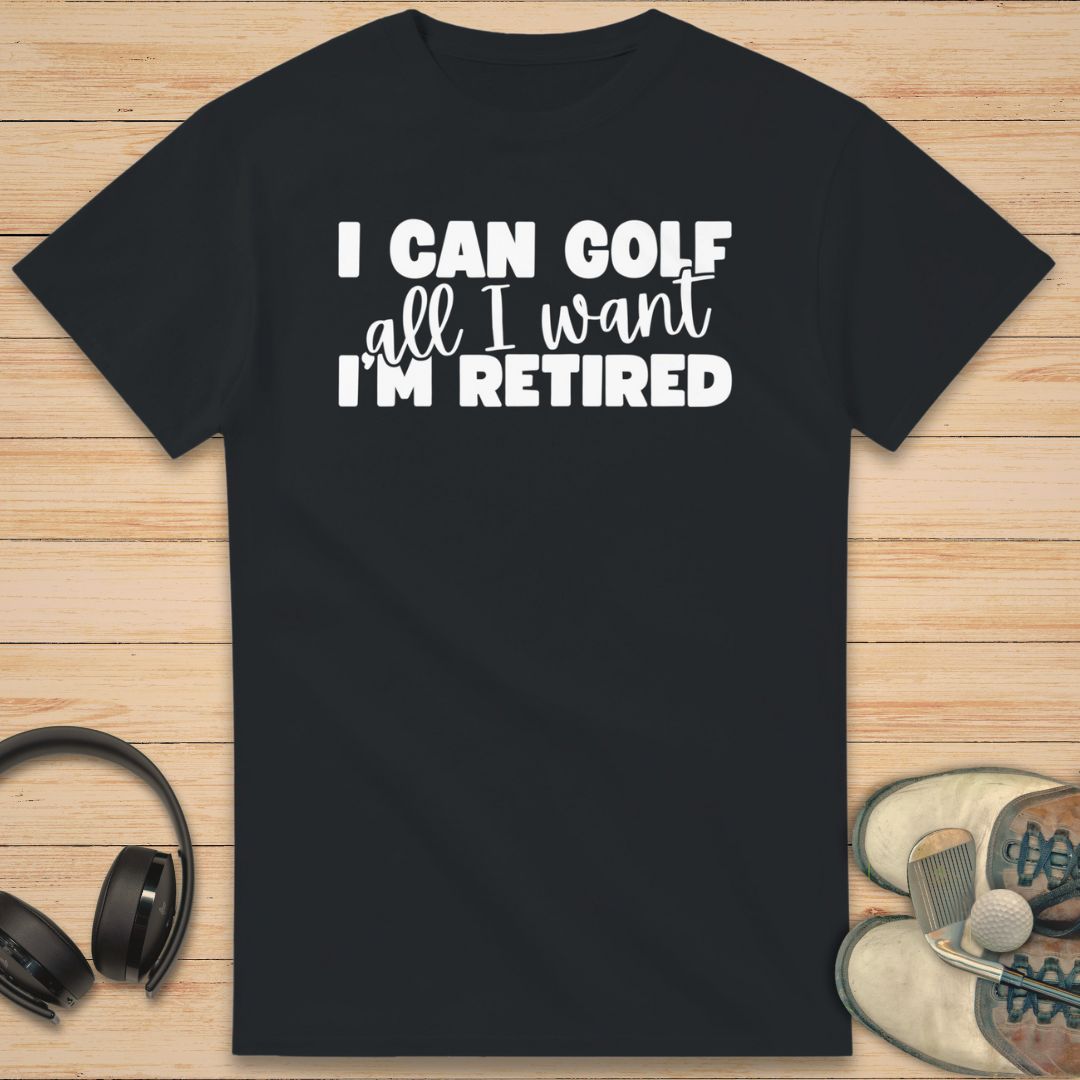 Golf All I Want T-Shirt in Black on a light wooden floor lying next to headphones and golf shoes.