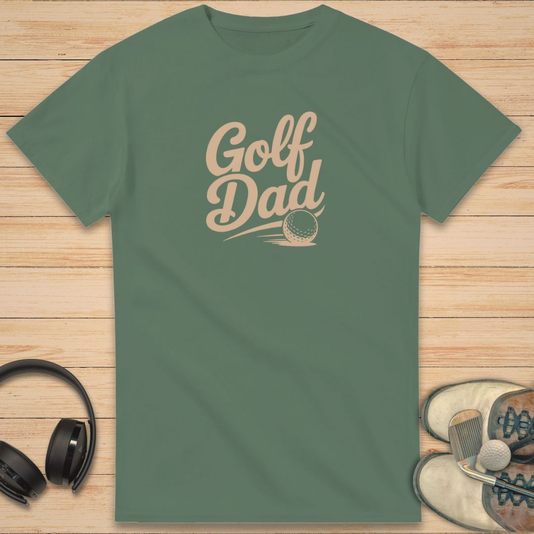Golf Dad II T-Shirt in Military Green on a light wooden floor lying next to headphones and golf shoes.